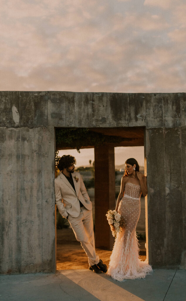 Couple looking at each other at sunrise, during their elopement, leaning against the wall at Paradero in Todos Santos.